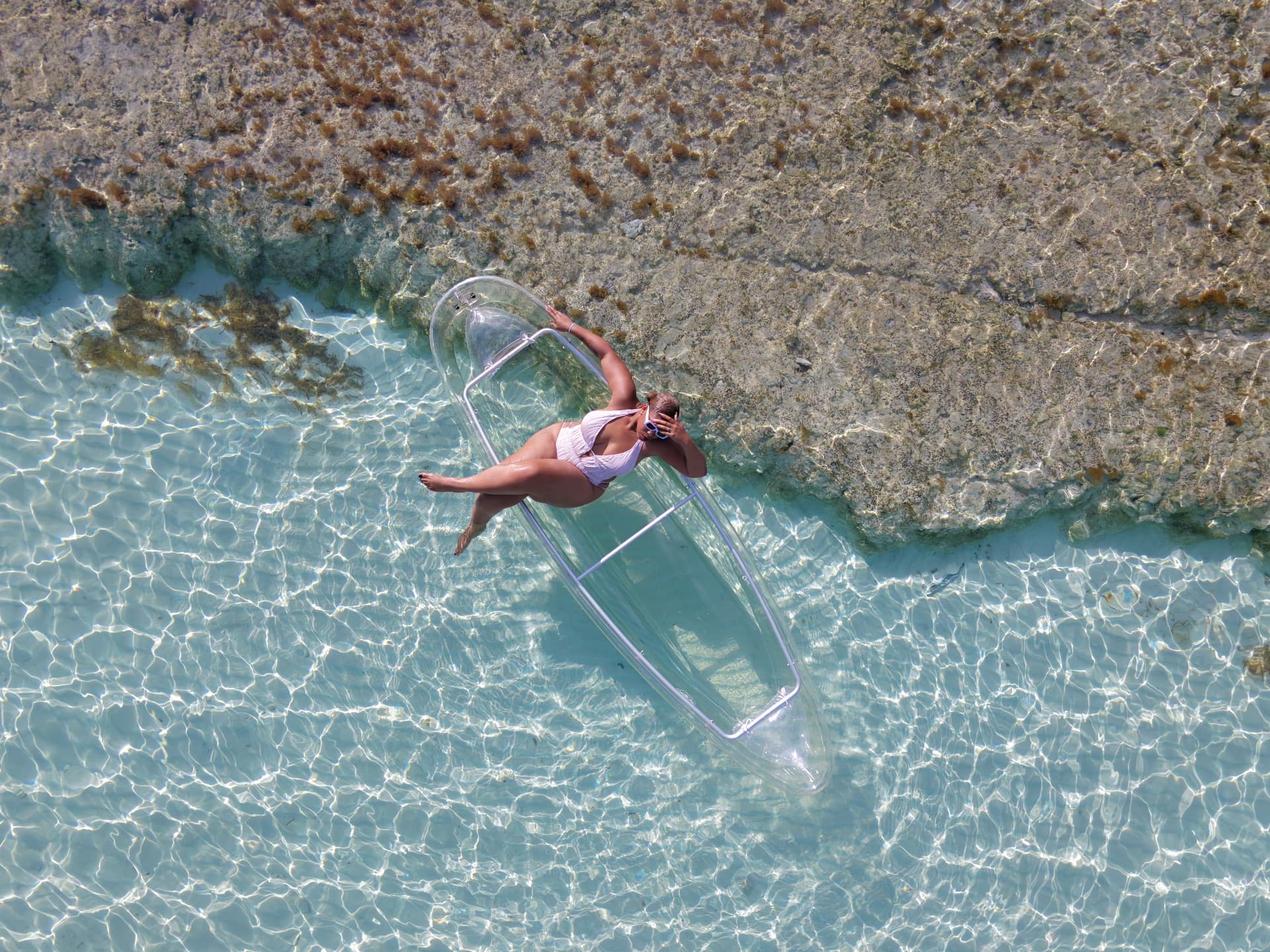 Aerial photograph of a guest in a clear kayak at the edge of a reef