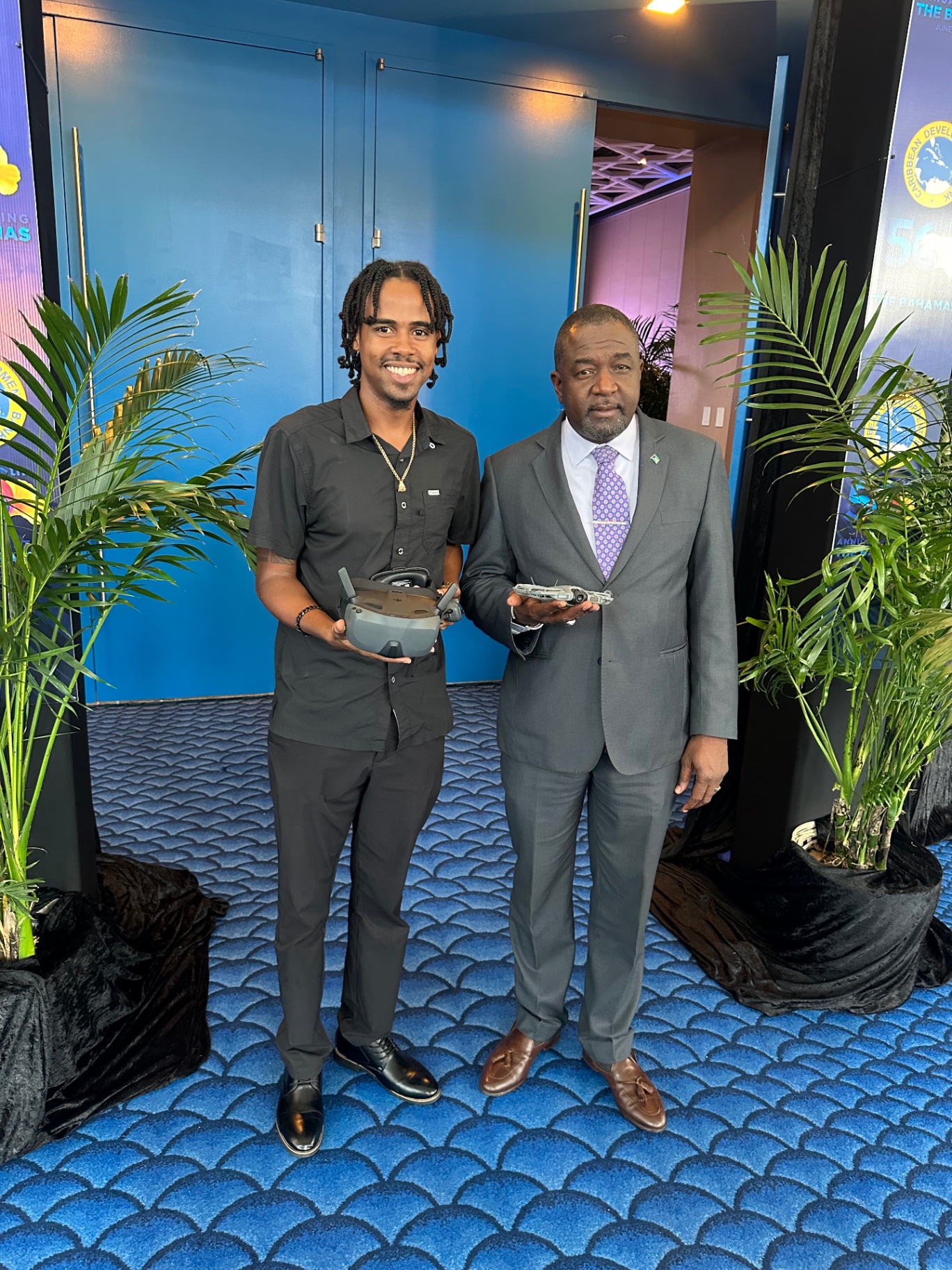 Andrick Wright standing beside a government official holding a drone controller and a small unmanned aircraft at a regional development event