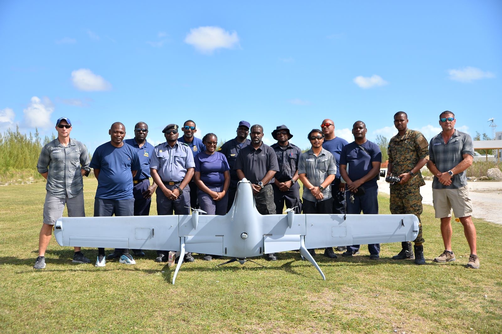 Group photograph of a training cohort standing behind a fixed-wing unmanned aircraft on a field