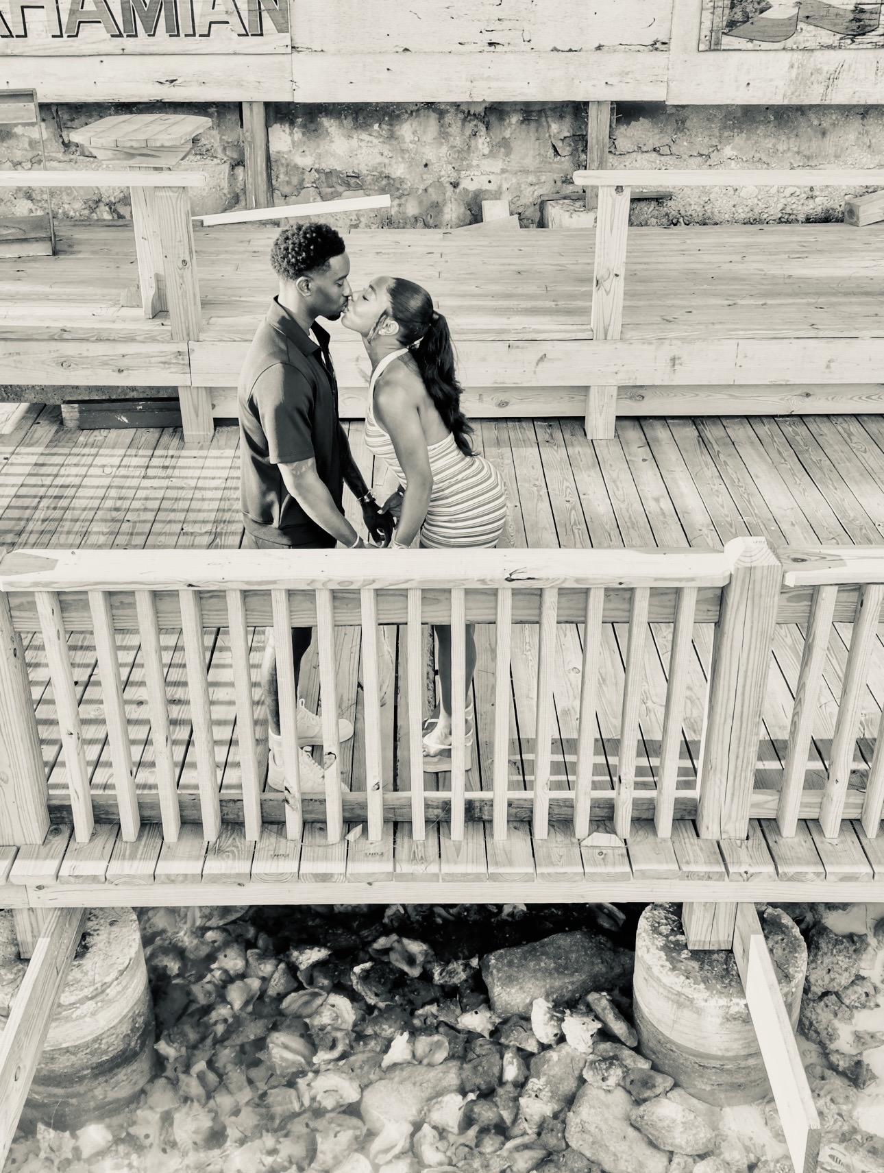 Black-and-white aerial photo of a couple kissing on a wooden boardwalk
