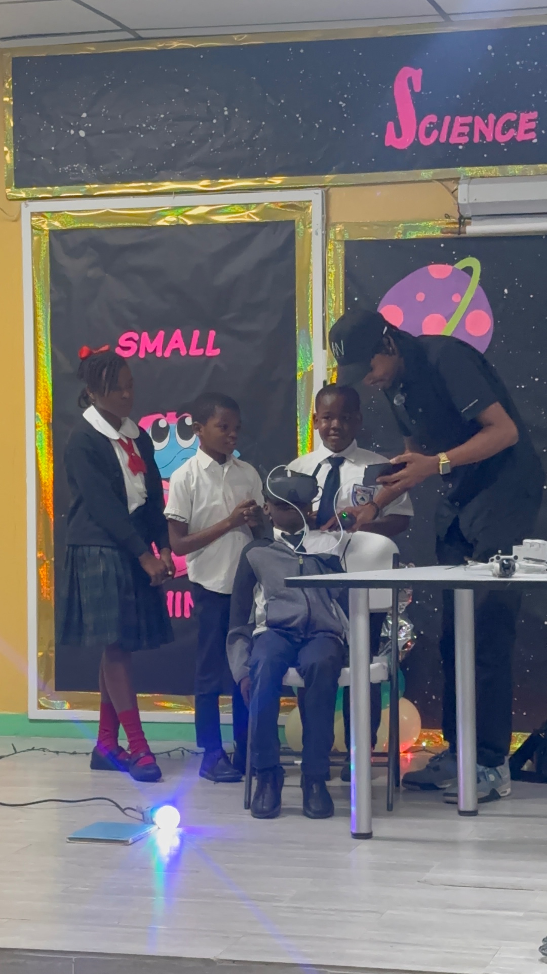 A student trying a virtual-reality headset while a FlyWright instructor guides the controls at a school science fair