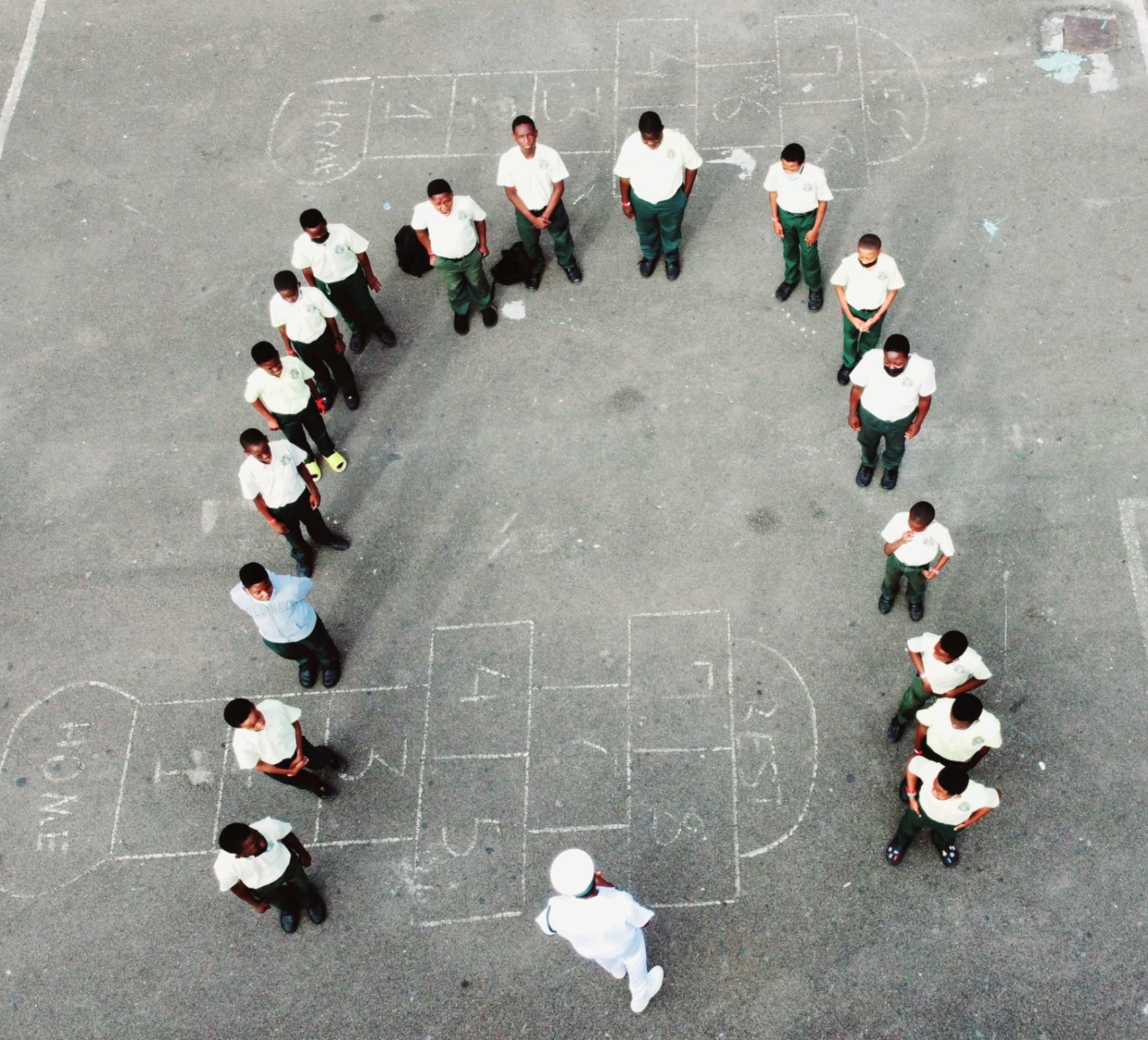 Aerial photograph of students forming a circle around chalk hopscotch grids in a schoolyard