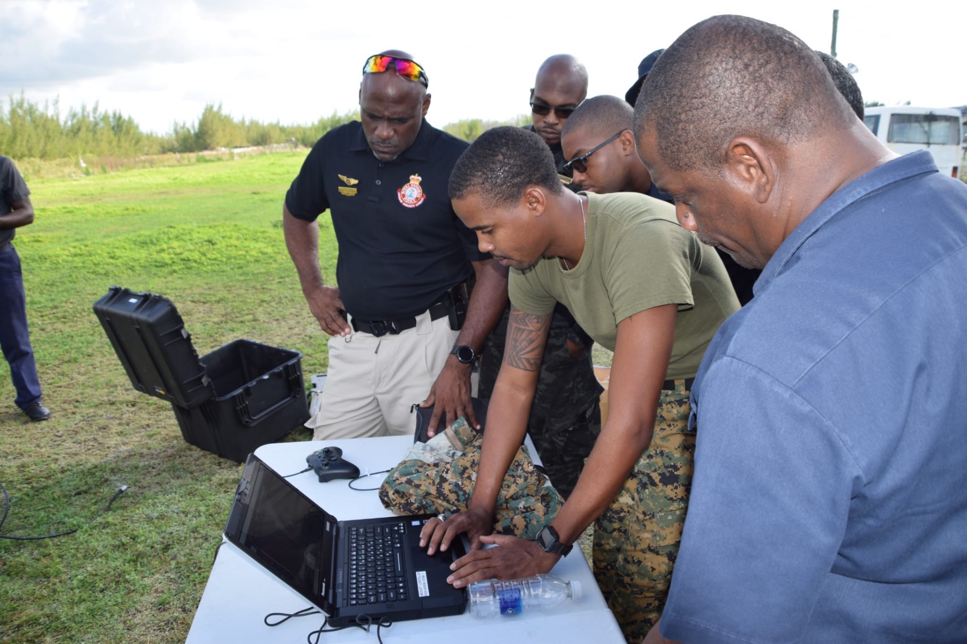 Trainees gathered around a laptop during a field training exercise in a grass field